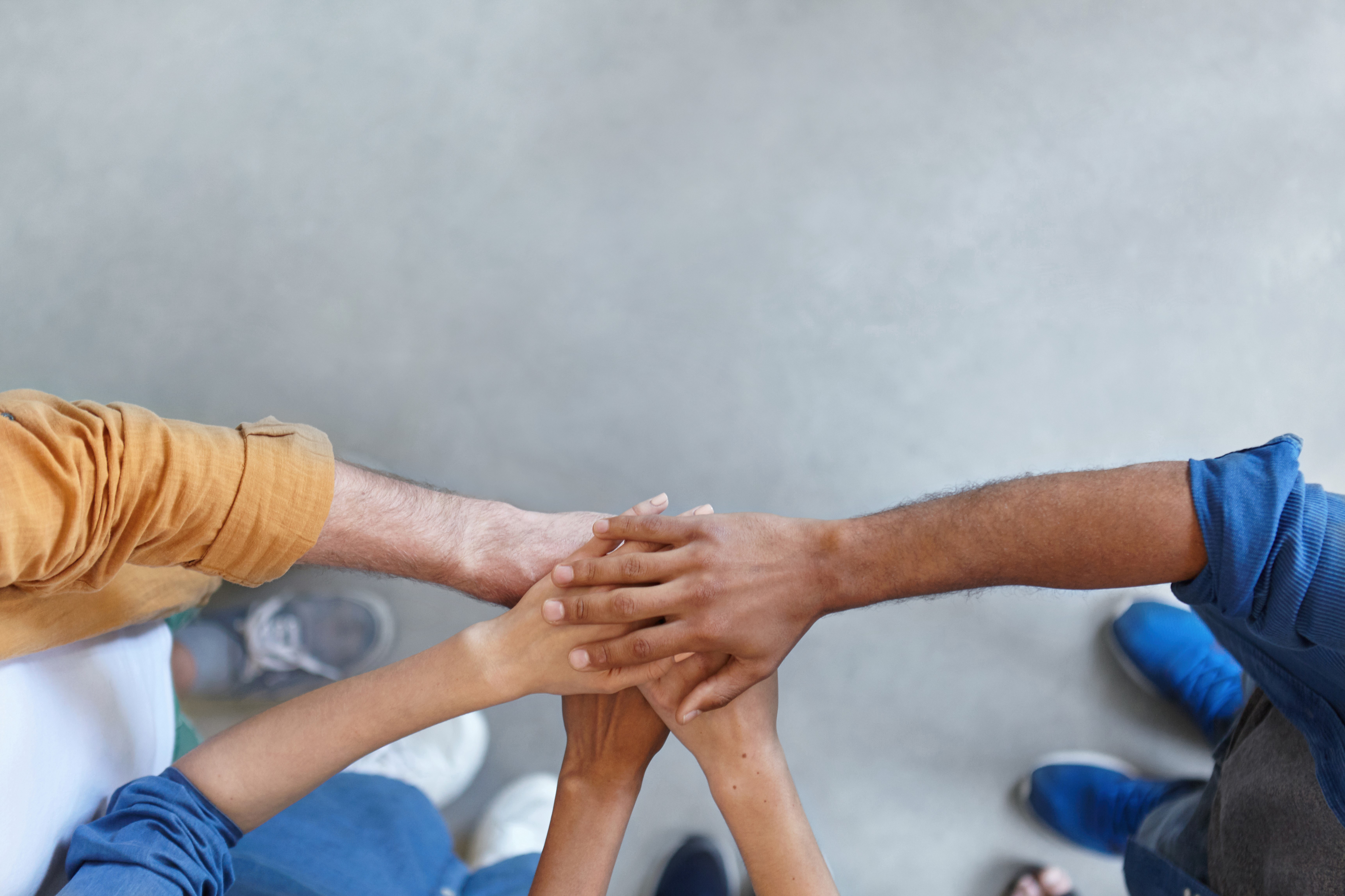 View from above of group of people keeping their hands in pile expressing social friendship, unity, agreement and support. Five people of different sexes collaborating showing their strength